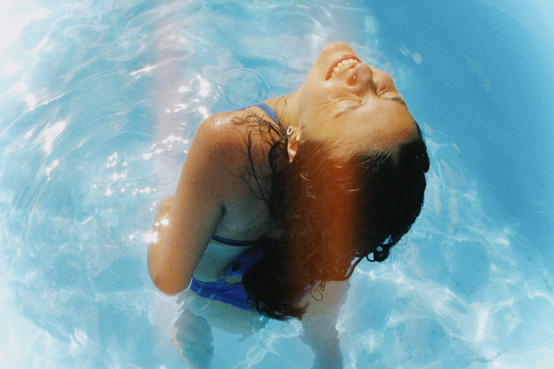 brunette woman standing with eyes closed in pool