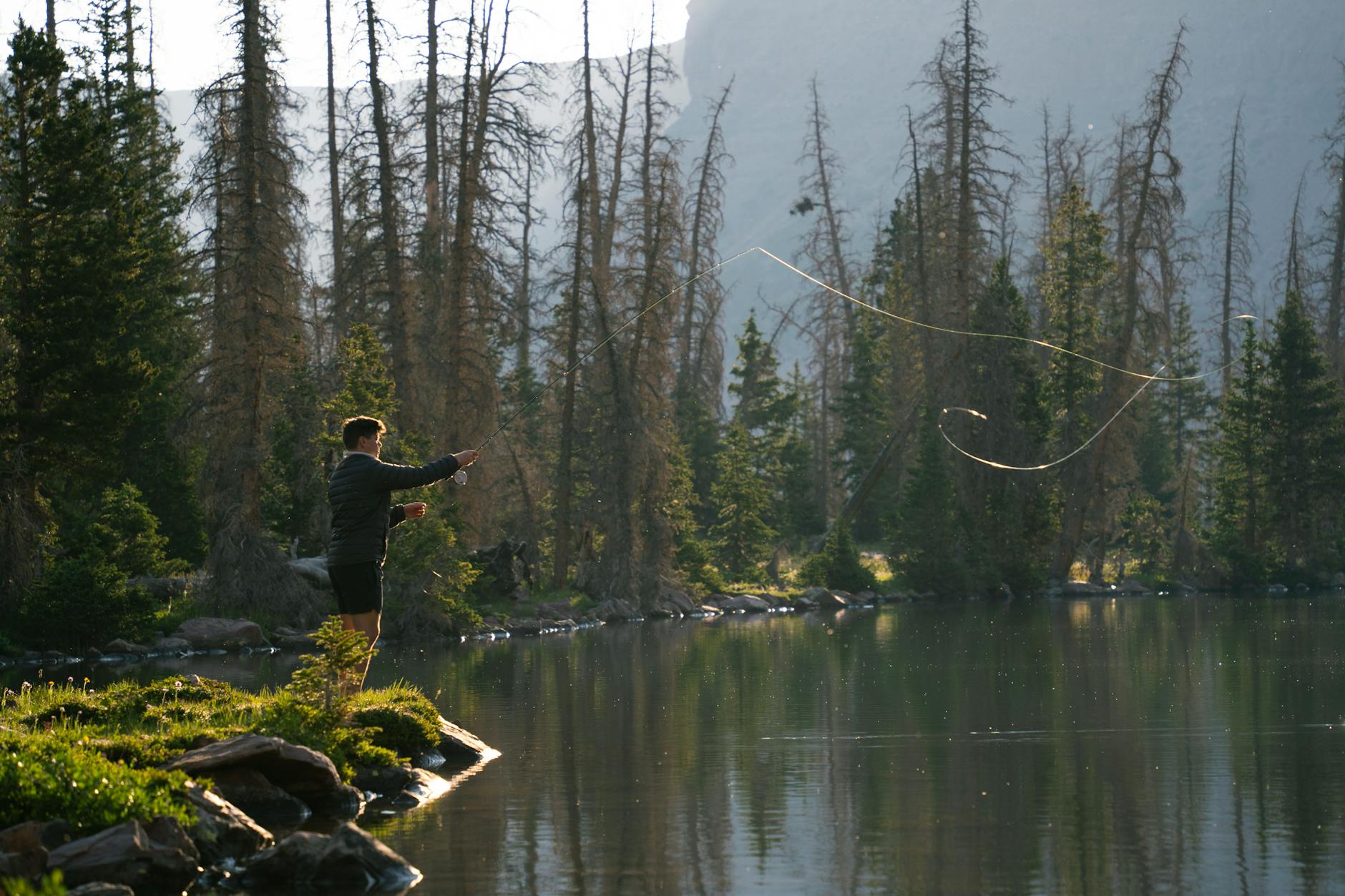 a man is fishing in a lake near a mountain